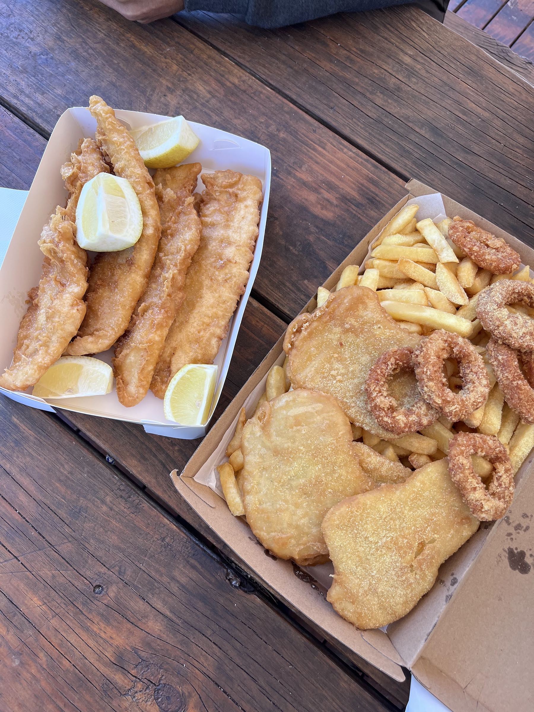 Battered fish with lemon, chips, calamari rings and potato cakes on an outdoor table